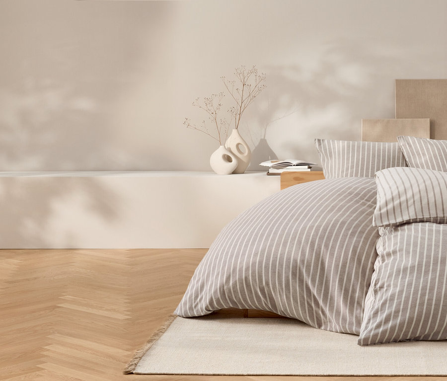 Schlafzimmer mit Bettwäsche mit Streifenmuster, Holzboden und dekorativen Vasen.