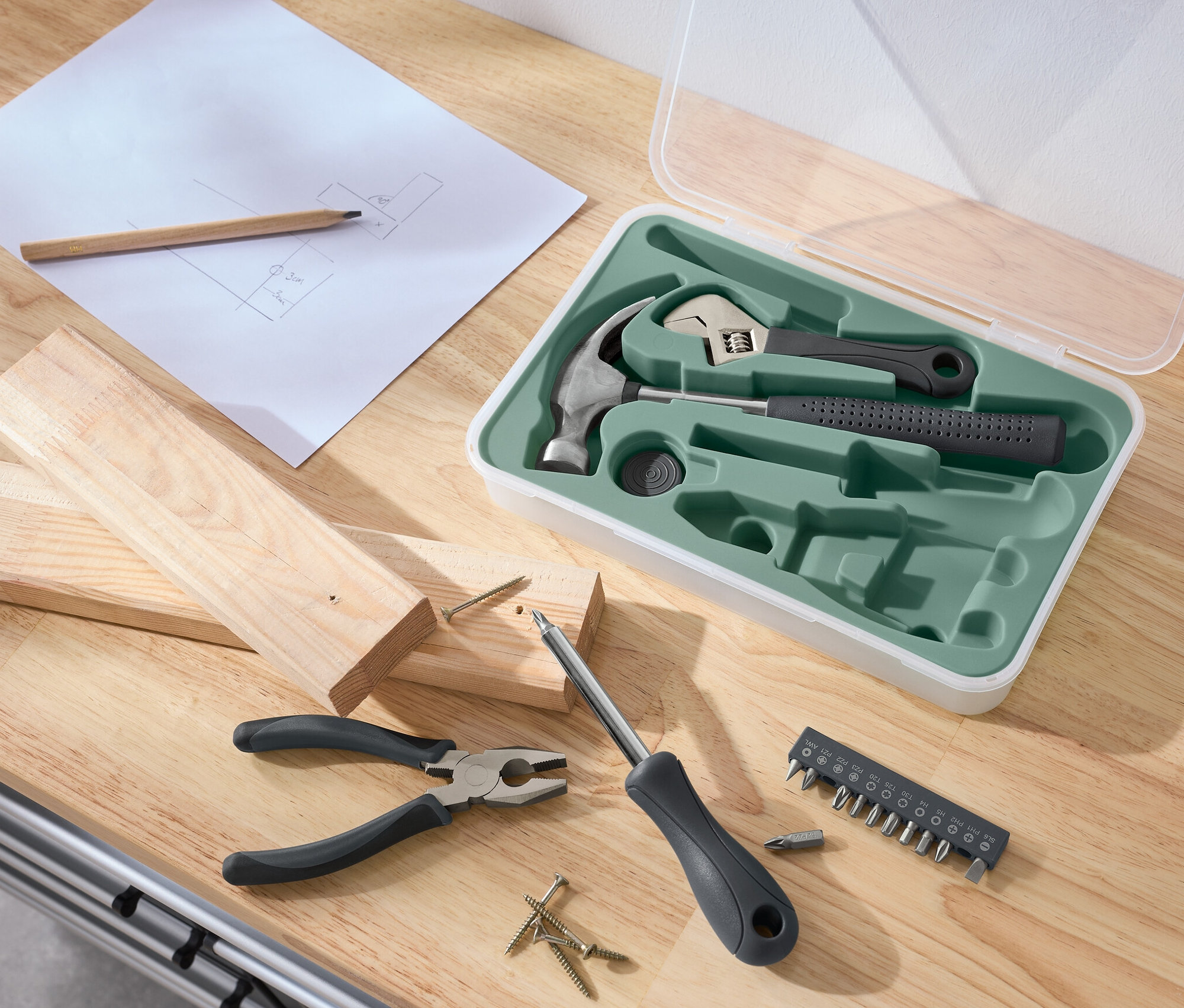 Auf einem Tisch liegen ein Werkzeug-Set, Holz, Schraubenzieher, Zange, Schrauben, ein Bleistift und eine Skizze.