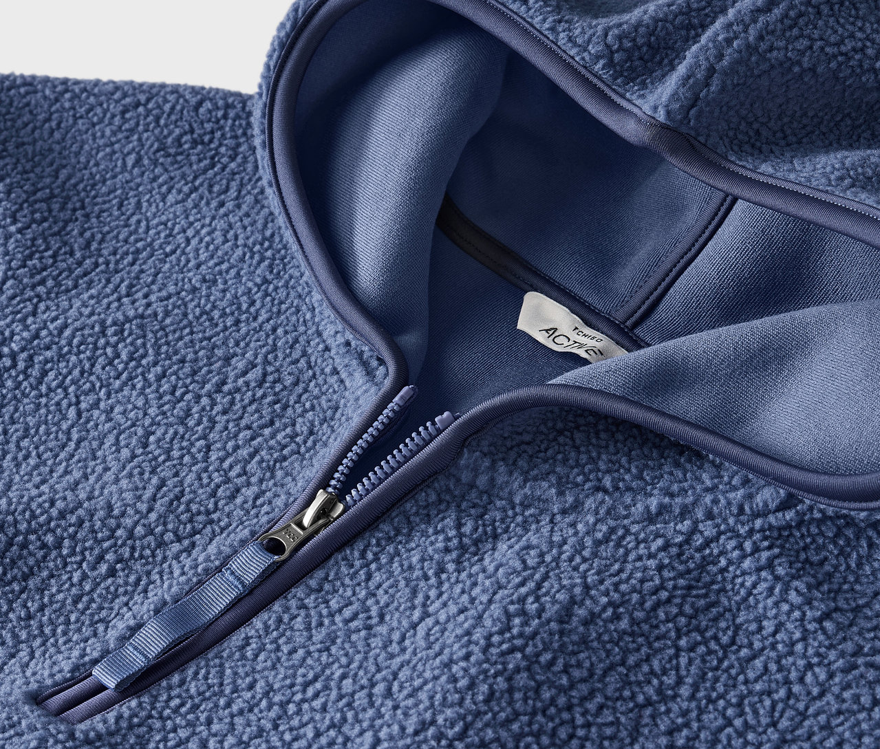 Detailaufnahme eines blauen Fleecepullovers mit Kapuze und Reißverschluss.
