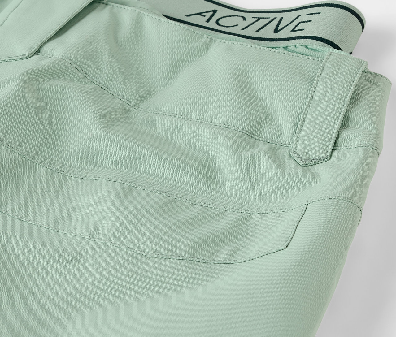Detailaufnahme einer hellgrünen Hose mit Tasche und Bund mit dem Schriftzug ACTIVE.