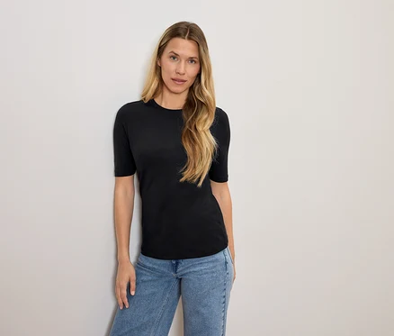 Frau mit blonden Haaren posiert in einem schwarzen T-Shirt und blauen Jeans.