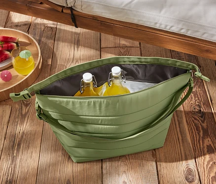 Eine grüne Kühltasche mit Flaschen und Wassermelone auf einem Holztisch.