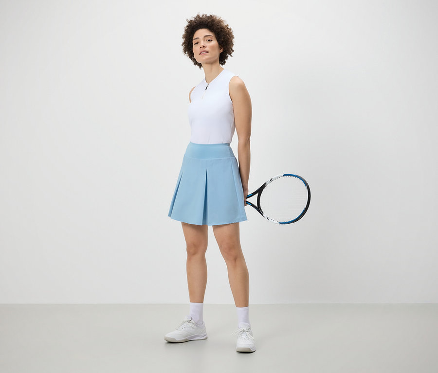 Frau posiert mit einem hellblauen Sportrock und einem Tennisschläger.
