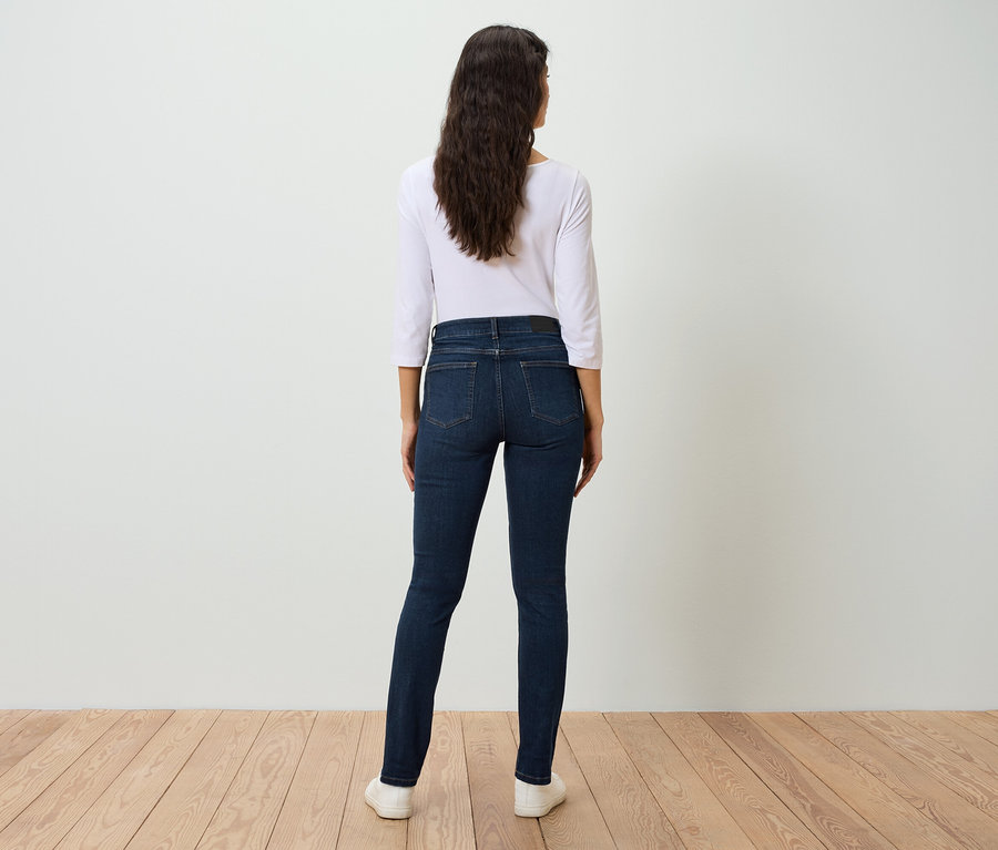 Eine Frau steht mit dem Rücken zur Kamera und trägt blaue Jeans und ein weißes Hemd.