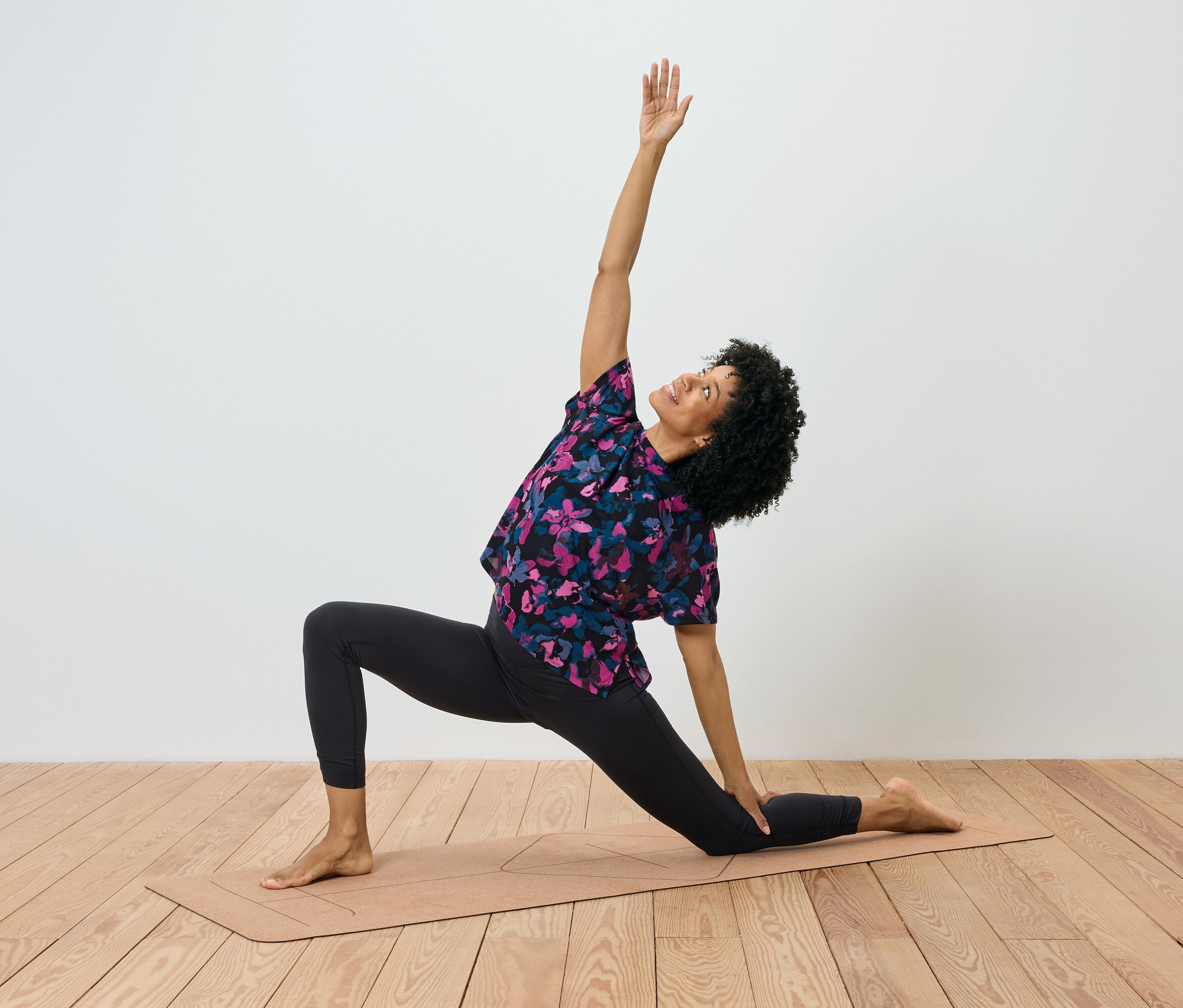 Frau mit lockigem Haar macht eine Übung auf einer Yogamatte, der rechte Arm ist erhoben und der linke berührt die Matte.