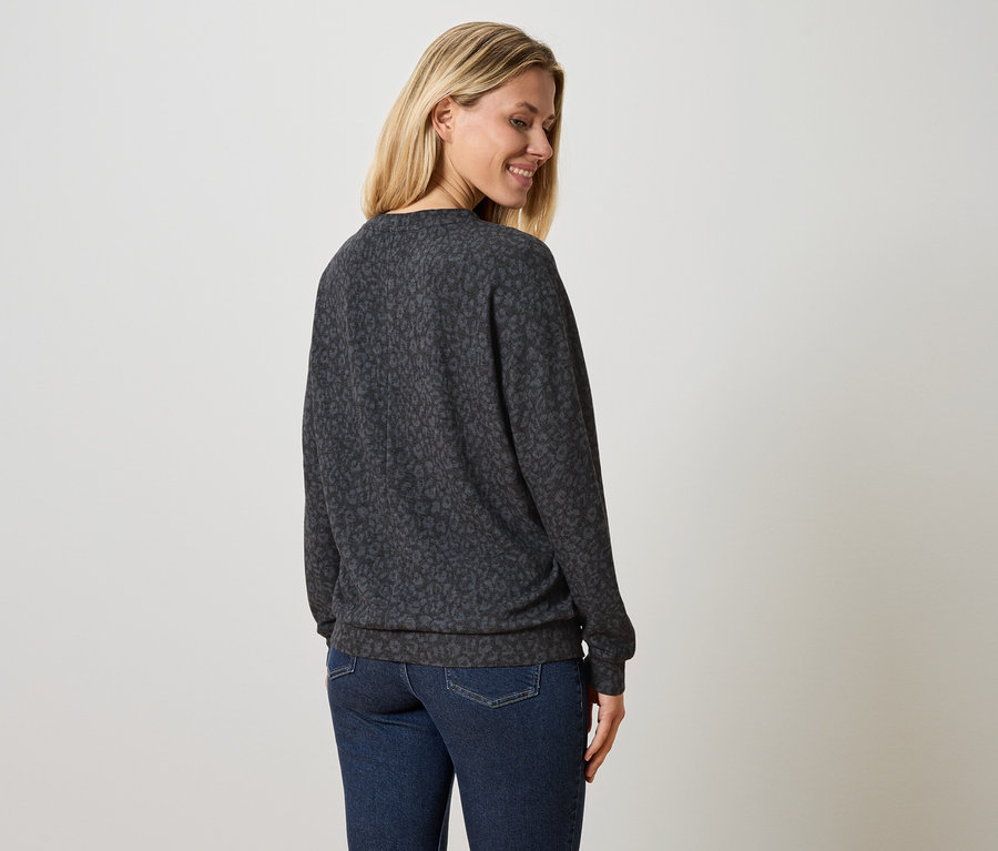 Frau trägt einen dunkelgrauen Pullover mit Leopardenmuster und blaue Jeans.