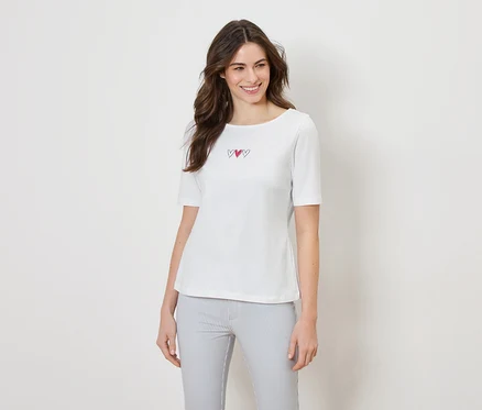 Frau trägt ein weißes T-Shirt mit drei Herzen und eine gestreifte Hose.