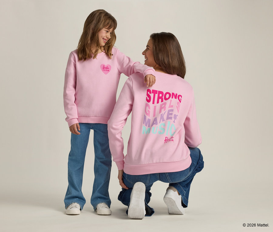 Mädchen mit Arm auf Schulter einer hockenden Frau, beide tragen rosa Sweatshirts und Jeans.