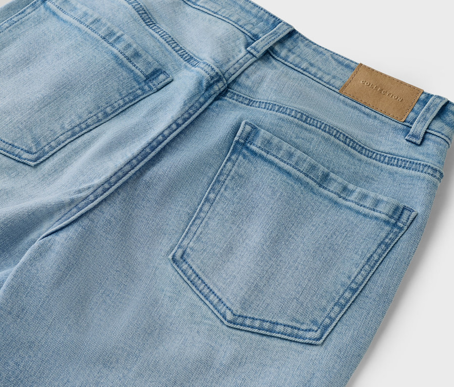 Nahaufnahme der Rückseite einer hellblauen Jeans mit Taschen und braunem 'Collection'-Etikett.