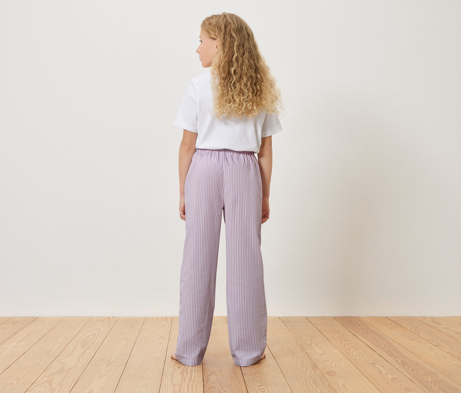 Rückansicht eines jungen Mädchens mit blonden, lockigen Haaren, das ein weißes T-Shirt und eine gestreifte, hellviolette Hose trägt.