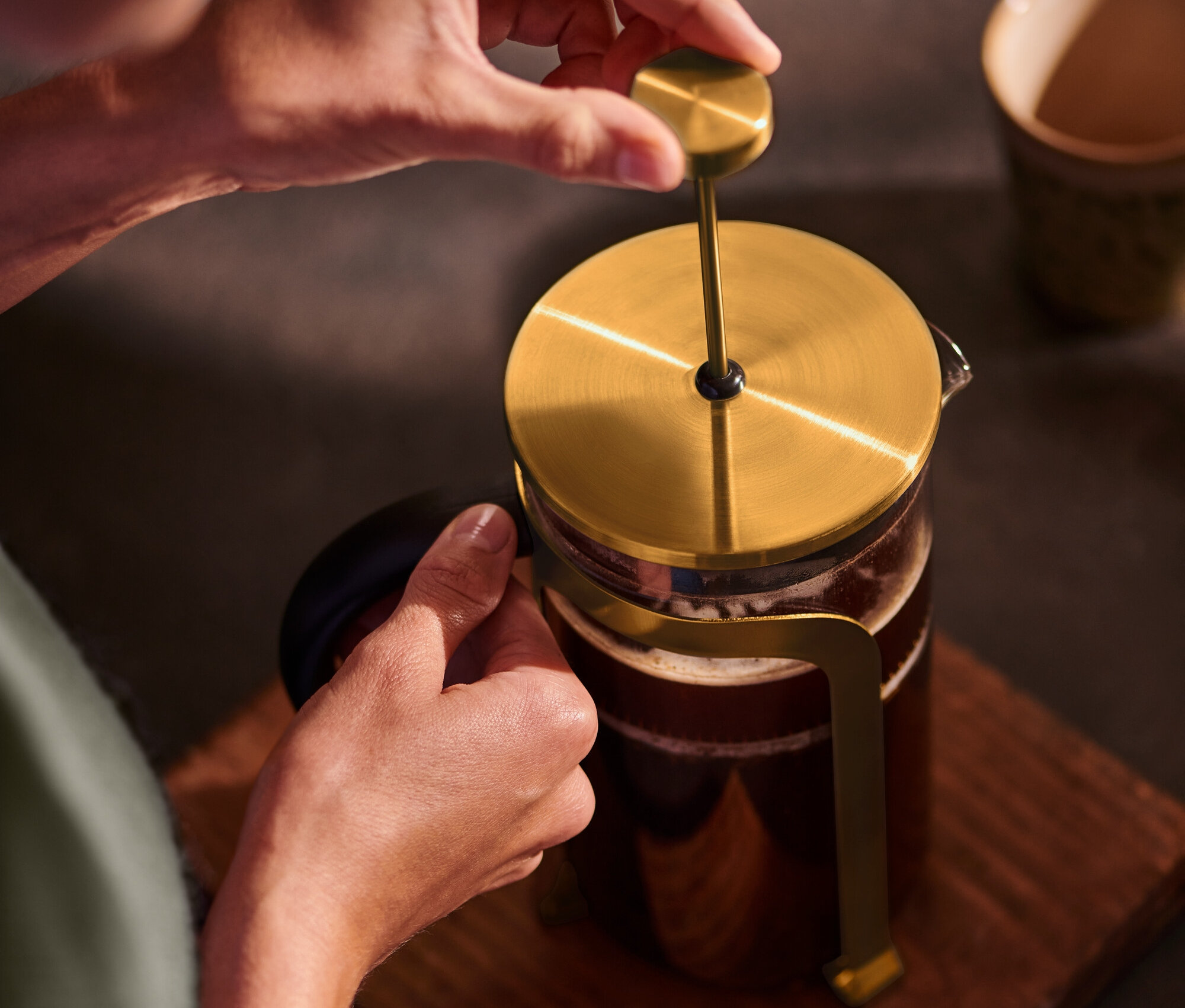 Eine Person drückt eine goldene Siebstempelkanne 800 ml für 6 Tassen auf einem Holzuntergrund.