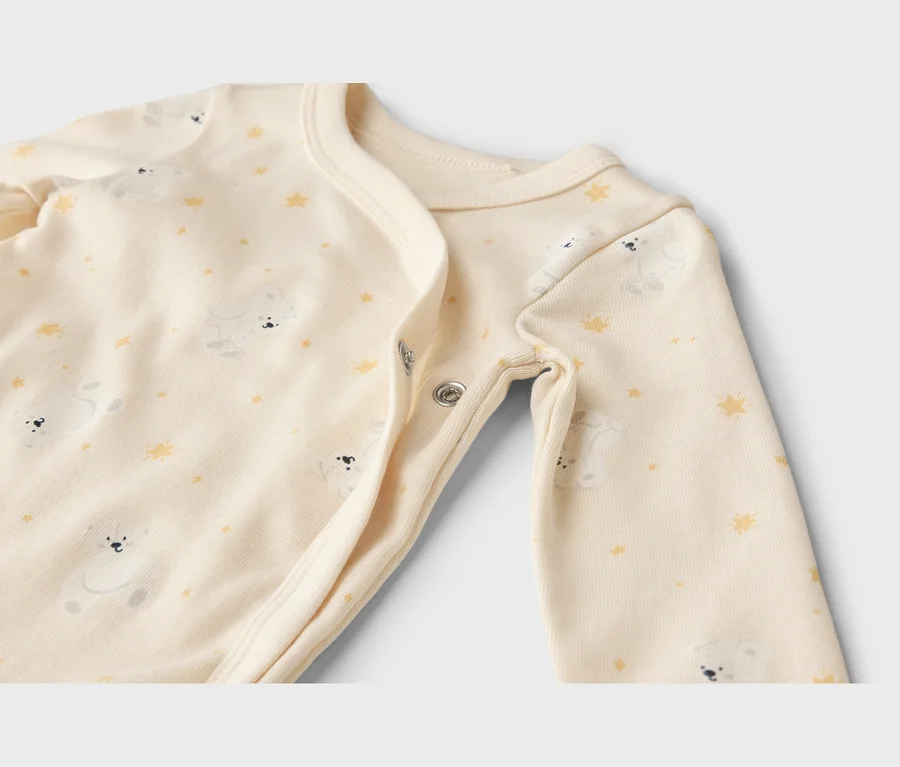 Nahaufnahme eines cremefarbenen Baby-Bodys mit weißen Bären und gelben Sternen, der Druckknöpfe hat.