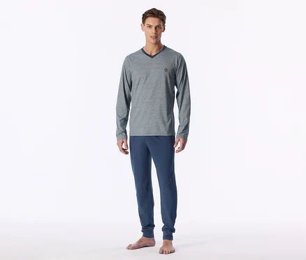 Mann steht barfuß und trägt einen grauen, langärmligen V-Ausschnitt-Pullover mit dunkelblauem Kragen und eine blaue Jogginghose.