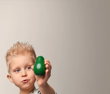 Ein Junge hält eine grüne Avocado und trägt eine Kleinkinder-Küchenschürze.