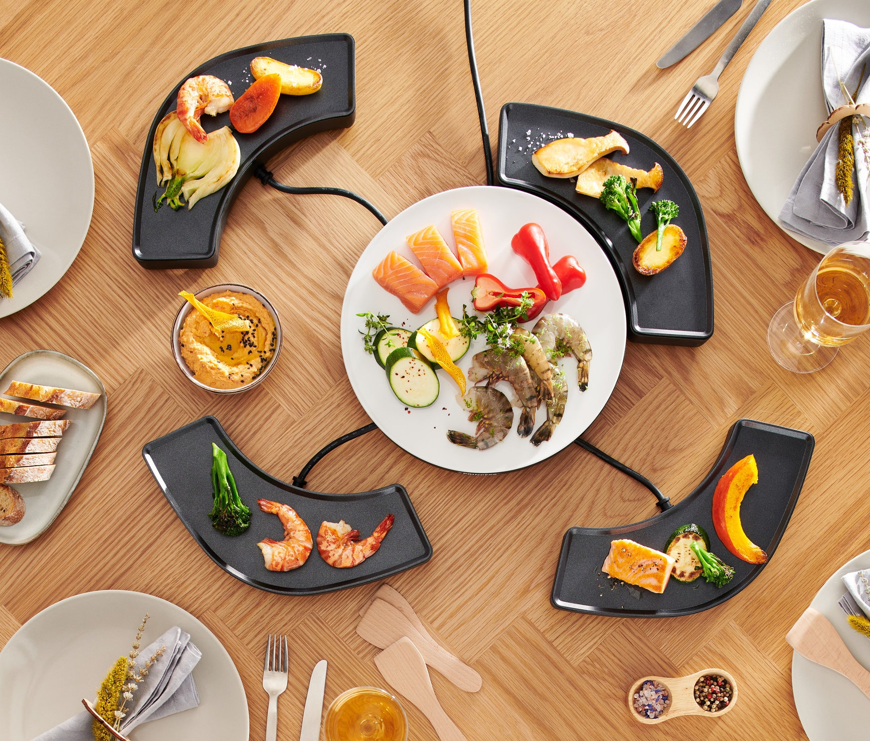 Draufsicht auf einen Tisch mit »Dinner4All« Tischgrill, Tellern, Speisen und Getränken.