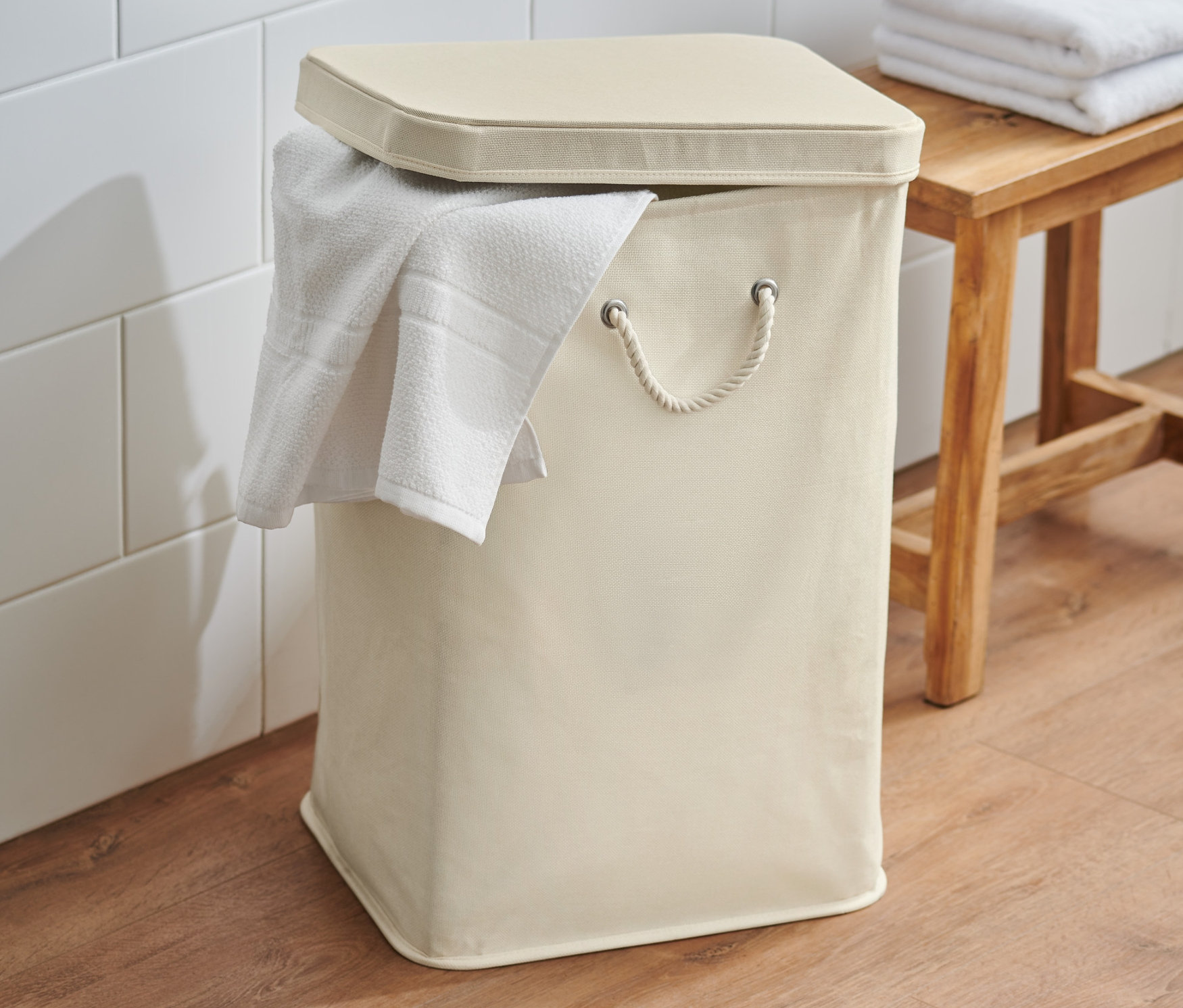 Ein cremefarbener Wäschesammler mit Deckel und Handtuch steht im Badezimmer.