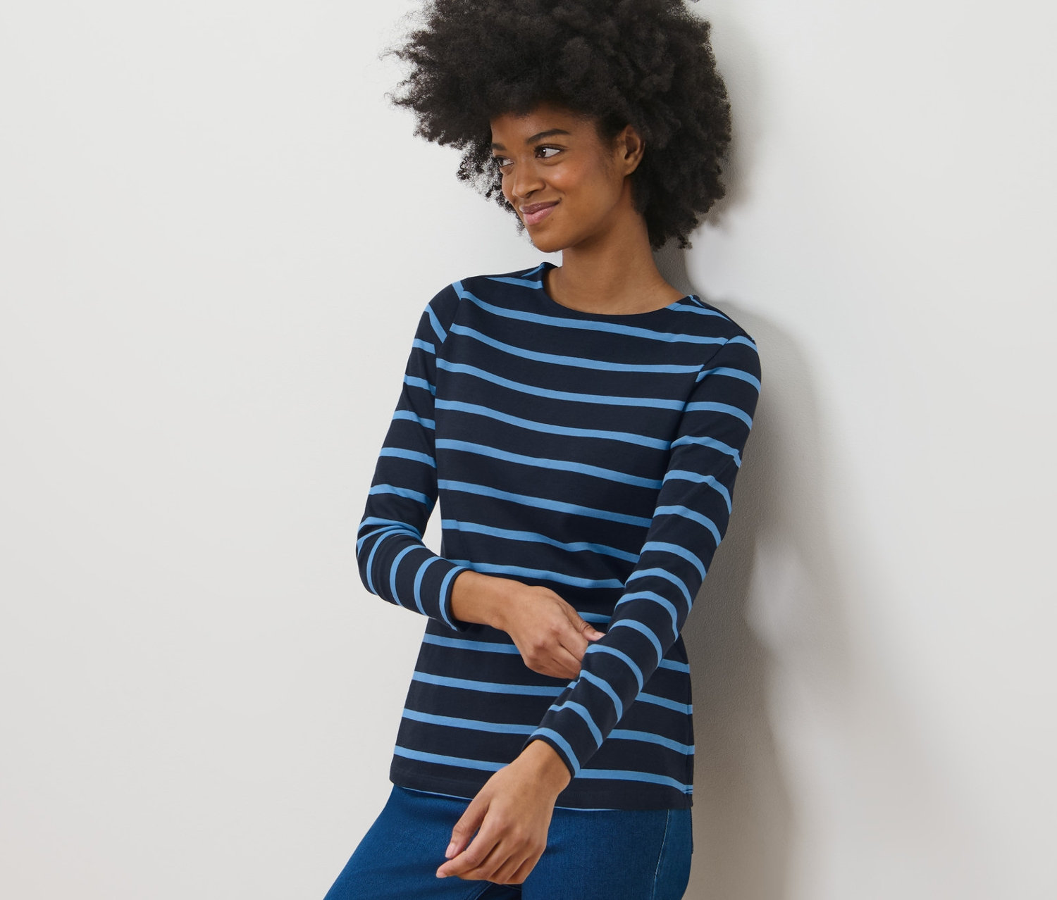Eine Frau steht an einer Wand und trägt ein dunkelblaues, gestreiftes Langarmshirt.