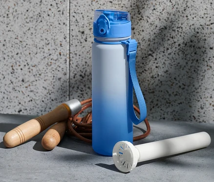 Eine blau-weiße Trinkflasche steht neben einem Springseil und einem weißen Kühlzylinder.