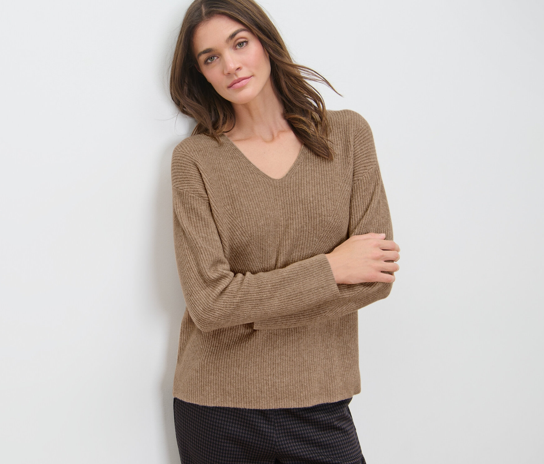 Frau an Wand gelehnt trägt camel Grobstrickpullover.