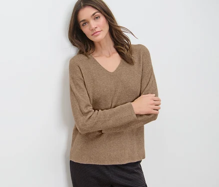 Frau an Wand gelehnt trägt camel Grobstrickpullover.