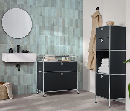 Im Badezimmer stehen eine schmale Kommode Metall »CN3« mit zwei Schubladen und 1 Klappenfach und eine Kommode Metall »CN3« mit 1 Schublade, 1 Klappenfach und Umrandung, sowie ein runder Spiegel »Ameca«.