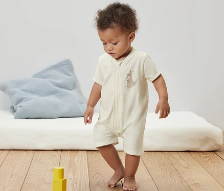 Kleinkind in kurzem Baby-Schlafanzug mit Känguru-Print steht auf Holzboden neben Holzbausteinen.