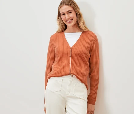 Frau posiert in orangefarbenem Cardigan mit Seide und weißer Hose.