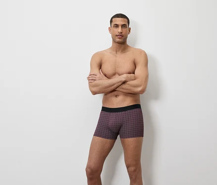 Mann posiert mit verschränkten Armen in Boxershorts mit geometrischem Muster.