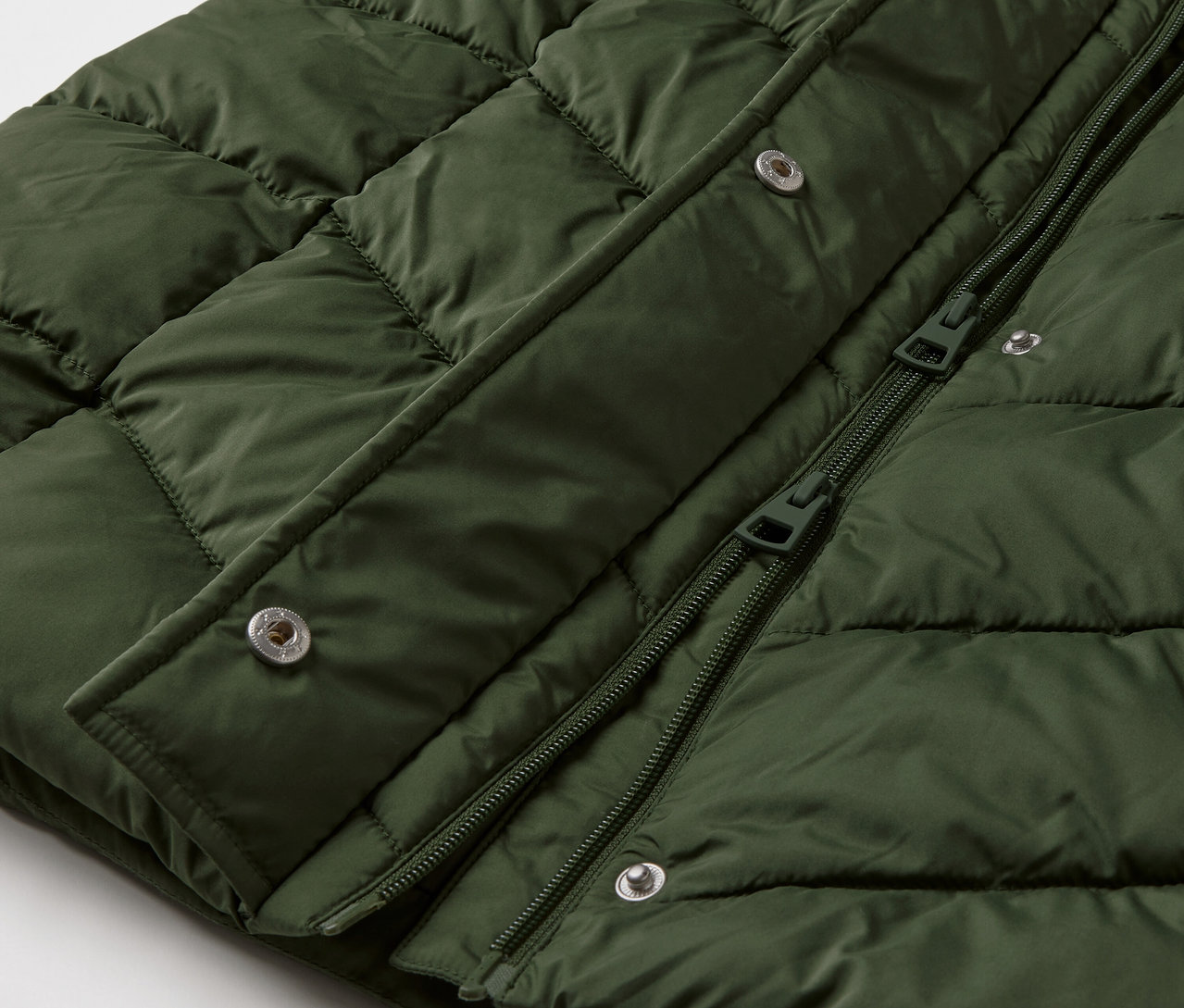 Detailaufnahme eines dunkelgrünen Steppmantels mit Kapuze.