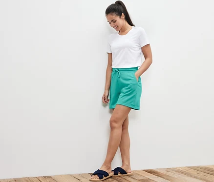 Frau steht mit Händen in den Taschen der Aqua Sweatshorts.