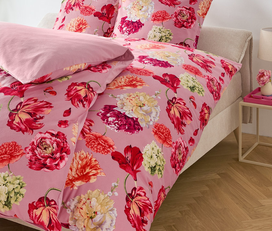 Rosa Bettwäsche mit Blumenmuster auf einem Bett.