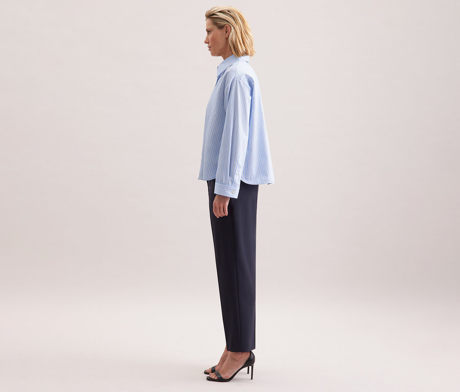 Frau von der Seite, die eine Seidensticker Oversize-Hemdbluse und dunkle Hosen trägt.