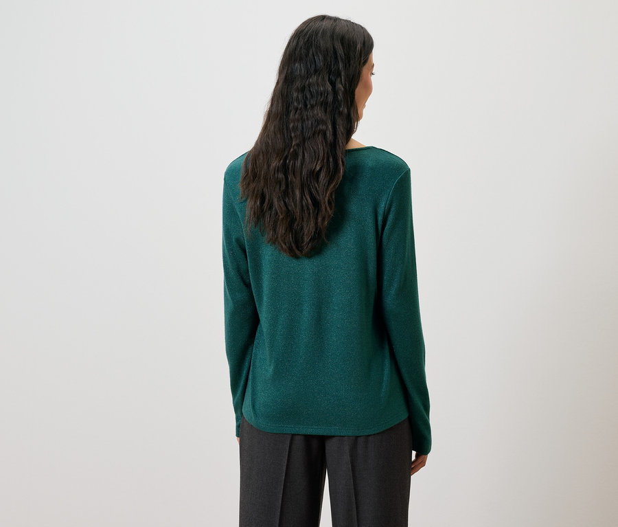 Rückansicht einer Frau mit langen, dunklen Haaren in einem grünen Pullover und grauer Hose.