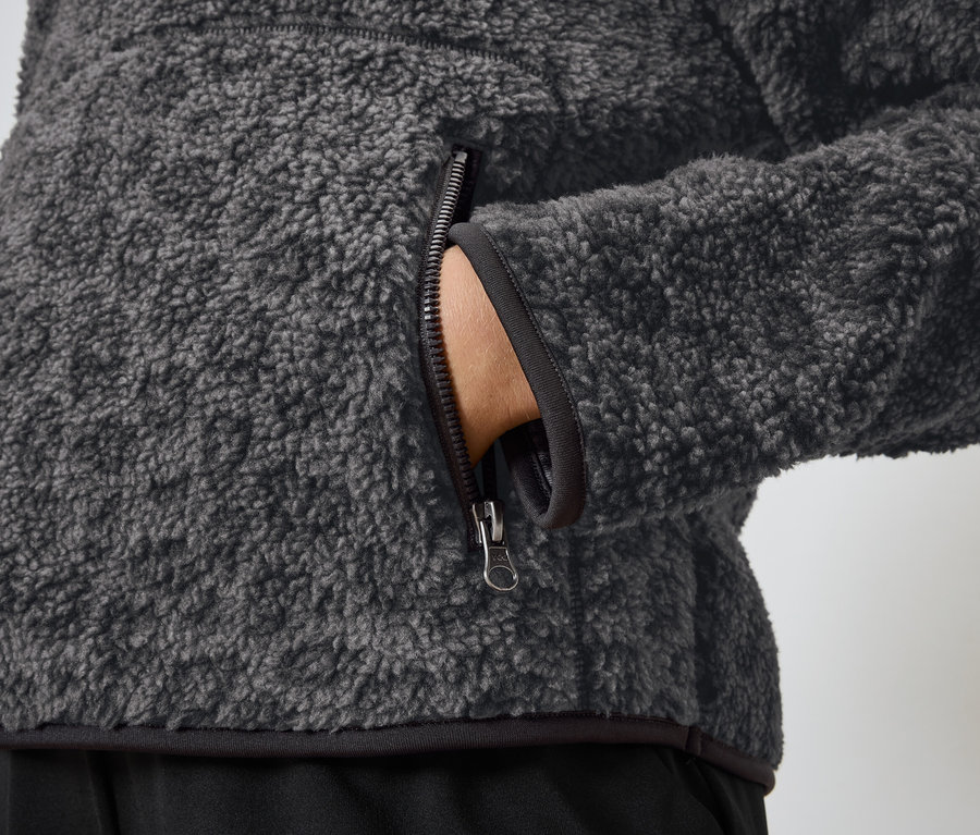 Detailaufnahme einer grauen Fleecejacke mit einer Hand in der Tasche.