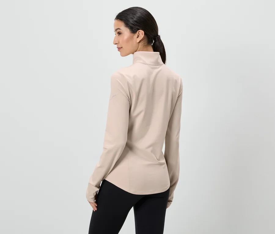 Frau von hinten, trägt beigefarbenes, langärmliges Oberteil und schwarze Leggings vor einem weißen Hintergrund.