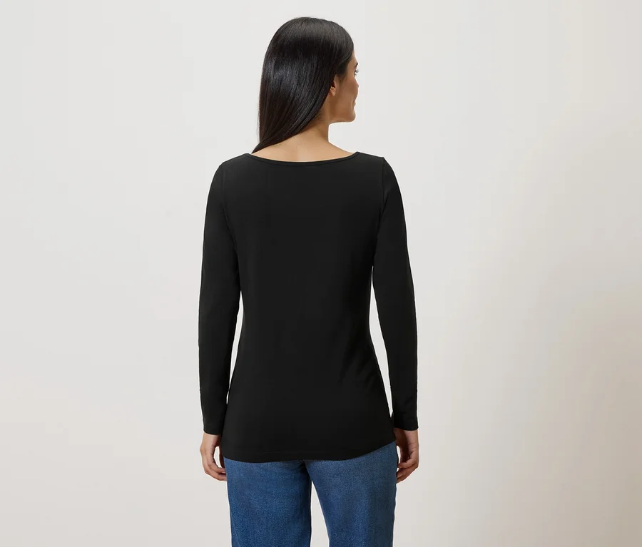 Frau von hinten in Jeans und schwarzem, langärmligem Oberteil vor hellem Hintergrund.