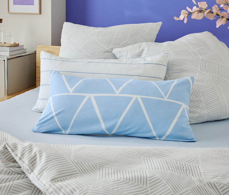 Nahaufnahme eines Bettes mit hellblauer Bettwäsche und mehreren Kissen mit geometrischen Mustern.