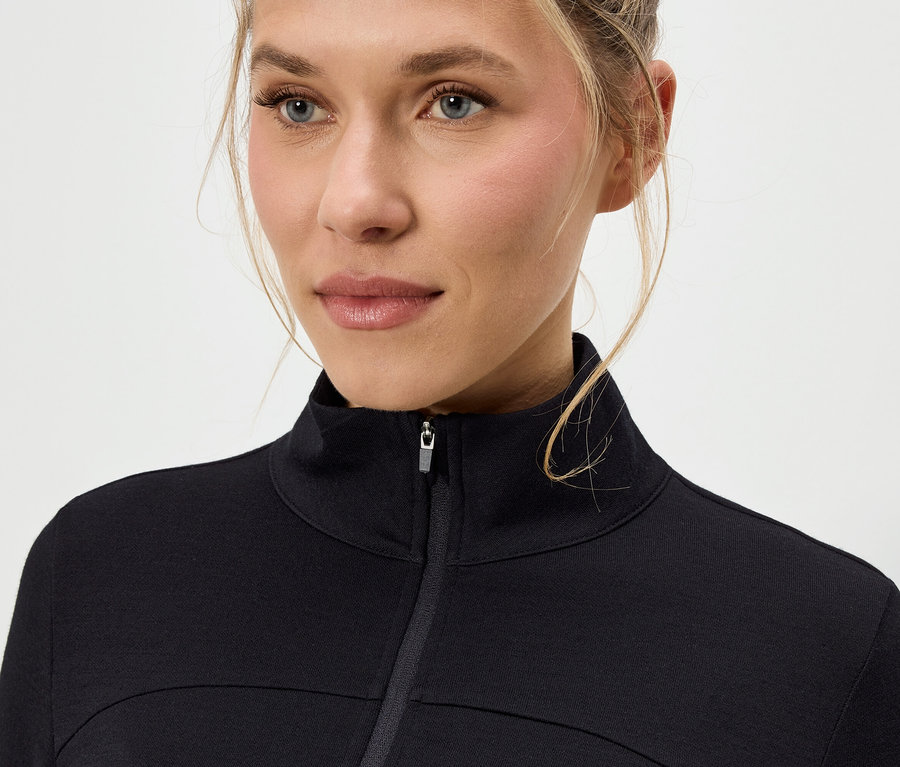 Nahaufnahme einer Frau mit blonden Haaren, die eine schwarze Jacke mit Reißverschluss trägt.