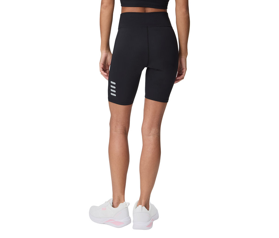 Frau von hinten in schwarzen Radlershorts mit vier reflektierenden Streifen und weißen Turnschuhen.
