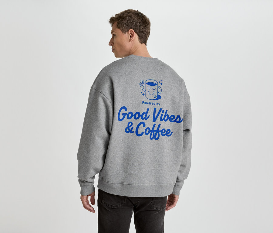 Mann von hinten in grauem Pullover mit blauem Aufdruck 'Good Vibes & Coffee'.