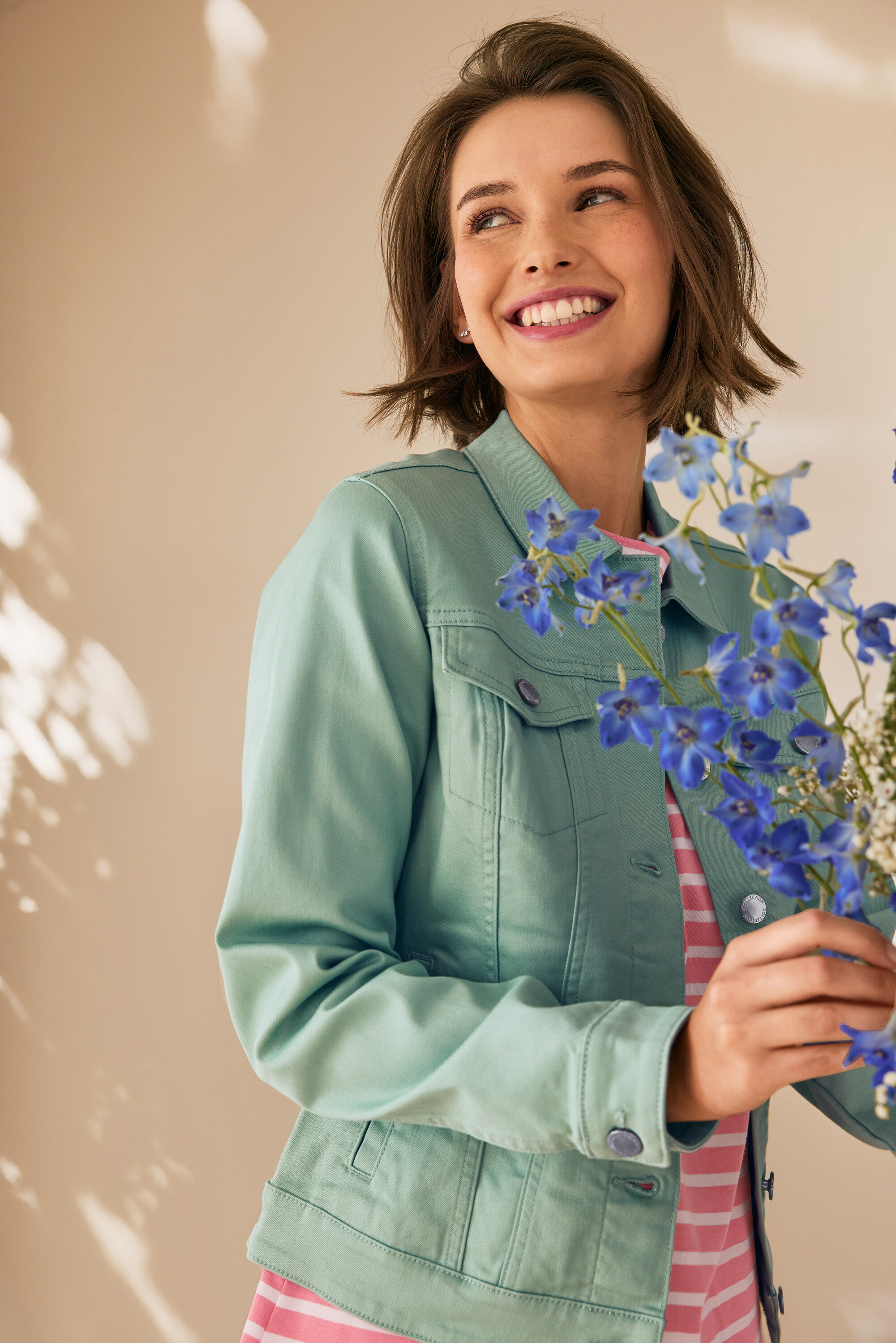 Frau lächelt und hält blaue Blumen, trägt eine mintgrüne Jeansjacke und 925 Silber Ohrstecker Zirkoniabogen.