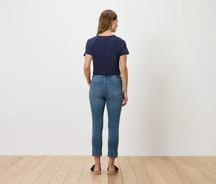 Rückansicht einer Frau mit blauem T-Shirt und Jeans vor einer weißen Wand.