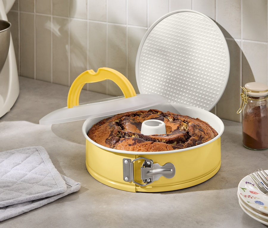Marmorkuchen in gelber Springform mit Deckel und Hebegriff neben Küchenmaschine und Gewürzglas