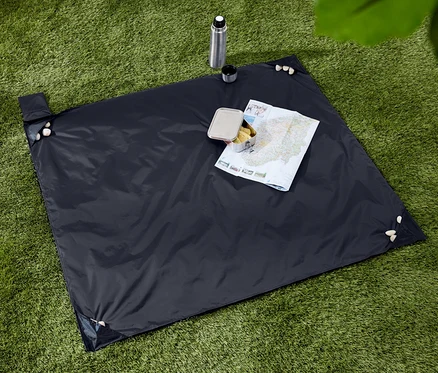 Dunkelblaue Picknickdecke mit Snacks, Thermoskanne und Karte auf einer grünen Grasfläche.