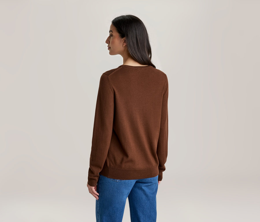 Eine Frau von hinten, die einen braunen Langarmpullover und blaue Jeans trägt. Ihr Kopf ist leicht nach links gedreht.