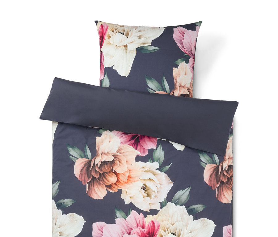 Bettwäsche-Set mit floralem Muster auf dunkelblauem Hintergrund mit großen rosa, cremefarbenen und pfirsichfarbenen Blüten. Ein schlichtes dunkelblaues Kissen liegt obenauf.
