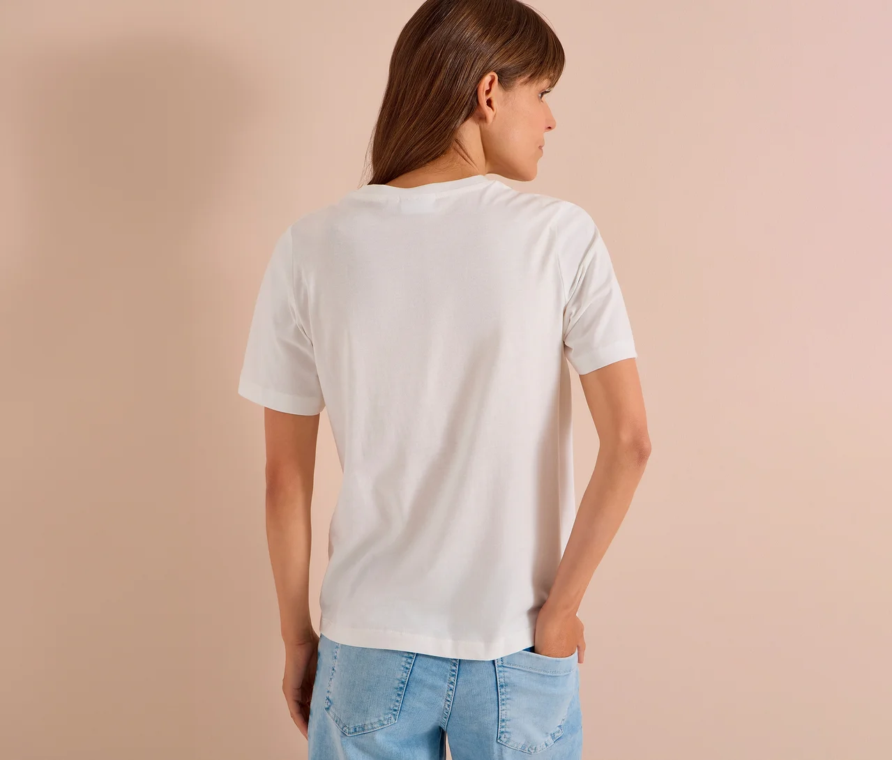 Frau von hinten in einem weißen CECIL Jerseyshirt und hellblauen Jeans, den Kopf nach rechts gedreht, eine Hand in der Gesäßtasche.