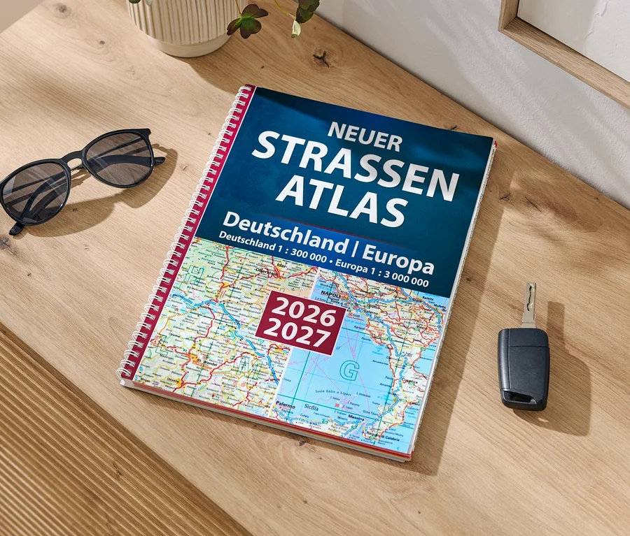 Auf einem Holztisch liegen eine schwarze Sonnenbrille, ein aufgeschlagener Straßenatlas und ein Autoschlüssel.