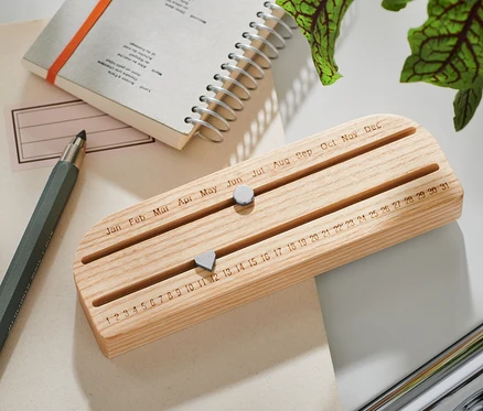 Ein Ewiger Kalender aus Holz liegt auf einem Tisch neben einem Block und einem Stift.