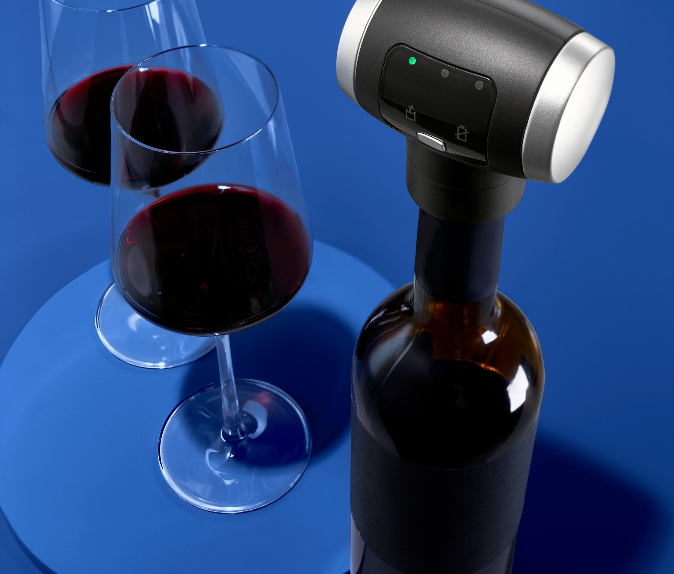 Zwei Gläser Rotwein neben einer Flasche mit einem elektrischen Vakuum-Weinflaschenverschluss.